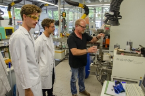 Mit der Unterstützung von Martin Althoff (r.) pressen und verkneten die Studenten Bagasse und ein Biopolymer miteinander, um dies anschließend in der Spritzgießmaschine weiterzuverarbeiten. (Foto: FH Münster/Frederik Tebbe)