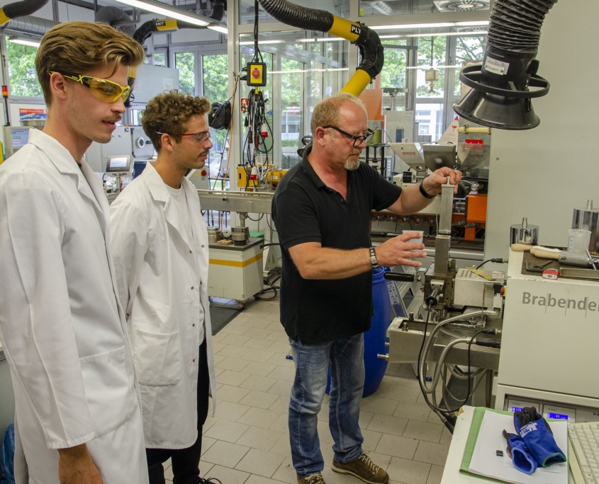 Mit der Unterstützung von Martin Althoff (r.) pressen und verkneten die Studenten Bagasse und ein Biopolymer miteinander, um dies anschließend in der Spritzgießmaschine weiterzuverarbeiten. (Foto: FH Münster/Frederik Tebbe)